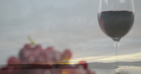 Showing tall wine glass half-filled with red wine at lakeside terrace, blurred grapes, copy space
