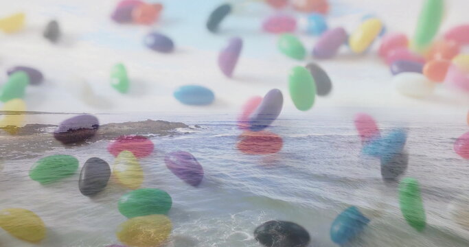 Floating cluster of multi-colored jelly beans drifting above rocky coastal shore, with ocean waves - Powered by Adobe