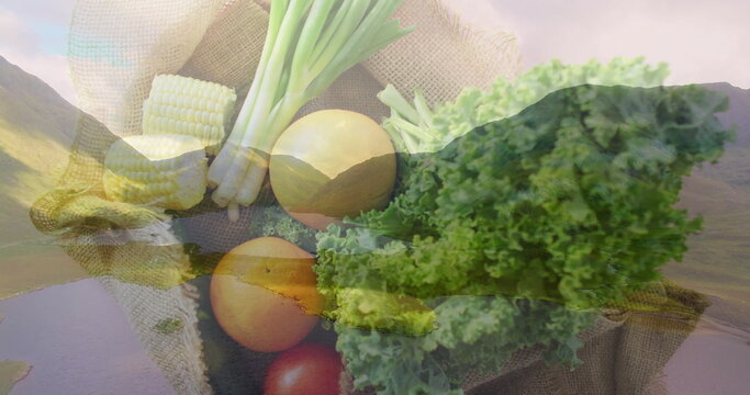 Fototapeta Displaying burlap sack holding corn cobs green onions kale tomatoes and onions over alpine valley