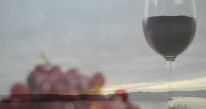 Fototapeta Showing tall wine glass half-filled with red wine at lakeside terrace, blurred grapes, copy space