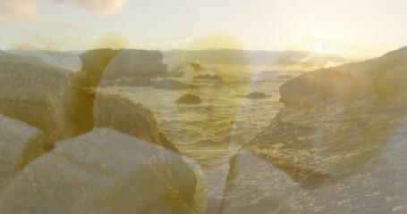Bathing rocky outcrop and waves in golden light from sun near horizon at shoreline, with boulders