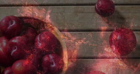 Displaying wooden bowl holding red plums on rustic wooden tabletop, with amber-orange overlay