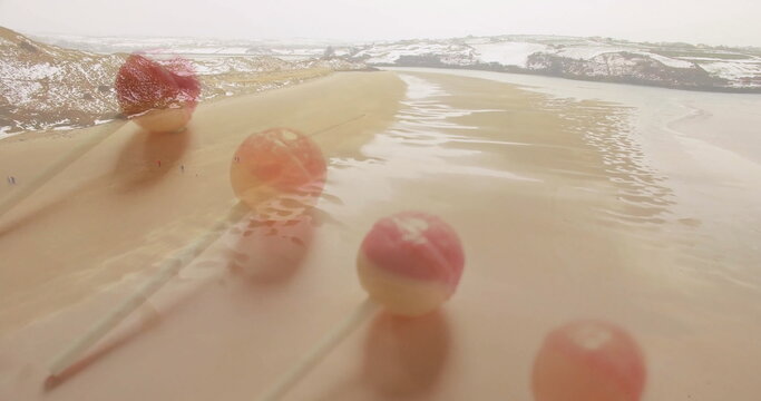 Fototapeta Standing five pink cream cake pops reflecting on coastal sand at low tide, with snow hills