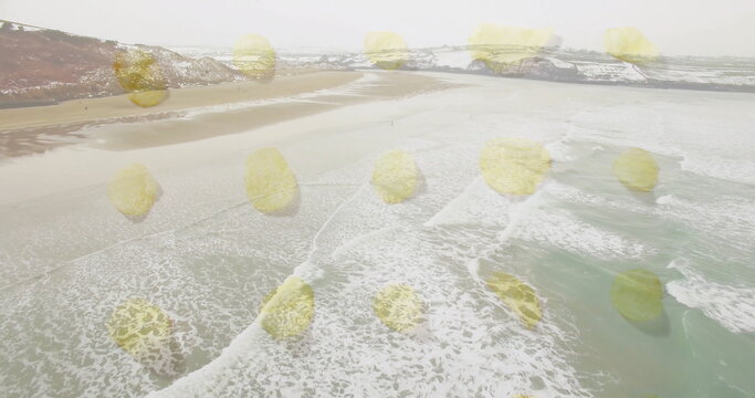 Fototapeta Overlaying yellow circle pattern on sandy beach at snow-dusted cliffs with ocean waves
