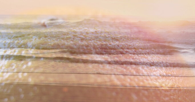 Fototapeta Rolling gentle ocean waves reflecting pastel sky at sunset on sandy shore, with sun glare