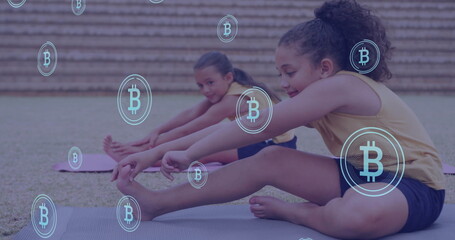 Reaching child on right touching toes on yoga mats on grass field, with floating Bitcoin icons