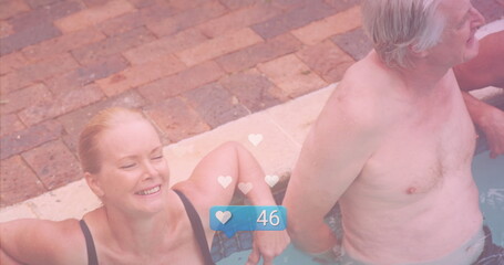 Smiling senior couple leaning on backyard pool edge, with digital heart icons and like counter