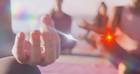 Holding woman's hand in meditation mudra on yoga mat at beach water's edge, with dawn glow