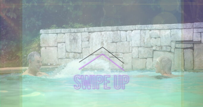 Two friends in swim trunks playfully splashing each other in outdoor private pool, with water jet