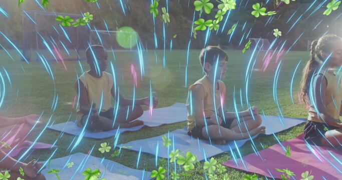 Fototapeta Sitting group of seven children in yellow tops and shorts meditating on grass, with yoga mats