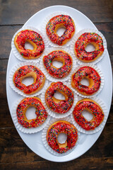 Top view flat lay of delicious donuts with red glaze and colorful sprinkles on a white plate, a...