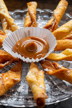 Traditional Colombian dessert platter featuring fried pastries (deditos) with powdered sugar, served with a delicious dipping sauce of Arequipe or Dulce de Leche on a glass plate.