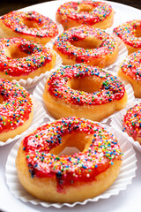 Top view flat lay of delicious donuts with red glaze and colorful sprinkles on a white plate, a...