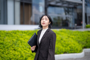 A woman in a business suit is walking down a sidewalk with a black briefcase