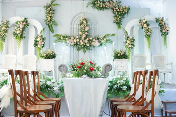 Refined Garden Wedding Stage with Floral Arches, Wooden Seating Rows, and Vibrant Red Centerpiece
