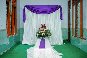Indoor Ceremony Setup with Purple Drapery, Floral Table Arrangement, and Green Carpet in a Calm...