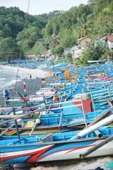 Cluster of Blue Fishing Boats on Rocky Beach with Flags and Coastal Village Background in a Busy...