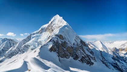 a towering snow covered mountain peak rises dramatically under a clear blue sky surrounded by rugged snowy ridges