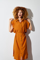 Stylish woman with curly hair in an orange dress, expressing excitement against a minimalistic...