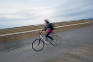 Blurred photo of a woman cycling on a street at sunset, capturing motion and urban life.. Alghero Sardinia, Italy