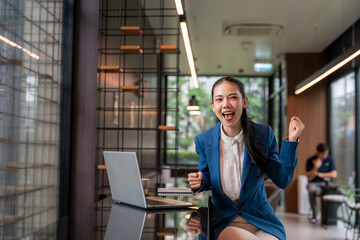 Excited businesswoman celebrating success while working on laptop in modern office