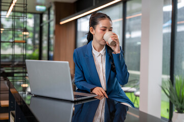 Businesswoman drinking coffee while working on laptop in modern office