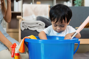 Curious Child. A toddler exploring a bucket of cleaning supplies with his mother nearby.