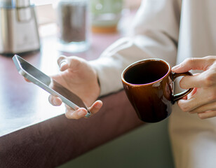 コーヒーカップとスマートフォンを持っている人の手元のアップ
