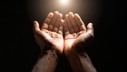 Close-up of cupped hands, illuminated by a bright light, against a dark background.