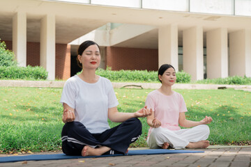 Two women practice yoga outdoors on mats sitting in a meditative pose in a serene setting