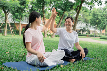 Women celebrating with a high-five after an outdoor workout in a grassy park on a sunny day