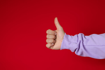 Male hand wearing a purple sweatshirt making a thumbs up gesture on a red background, approval...