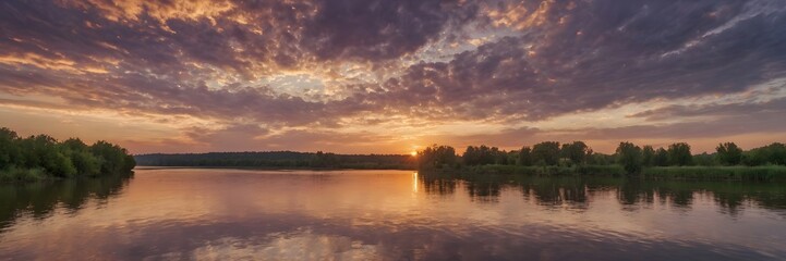 Obraz premium Serene Sunset Over Calm River with Vibrant Cloudy Sky and Lush Green Trees