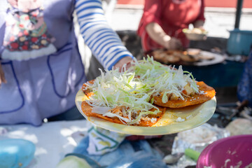 Una cocinera está vendiendo un plato con comida mexicana en una plaza pública.
