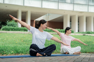 Two women practice yoga in a park stretching their arms wide for a balanced pose outdoors