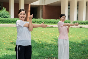 Two women stretching arms on the grass Active outdoor exercise to promote body fitness