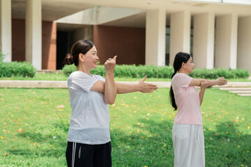 Two women stretching outdoors in a grassy area near a building promoting health and wellness