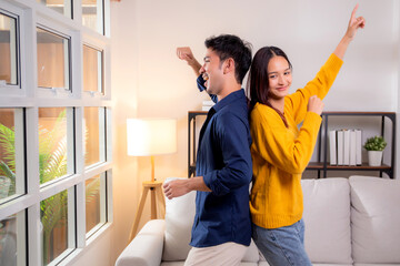 Young asian couple dancing playful together in cozy living room at home, smile and enjoy, joyful emotion and carefree, expression love and bonding, man and woman enjoy with fun and cheerful for relax.