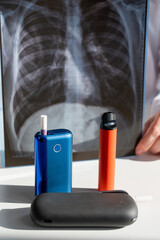 Doctor holds x-ray of lungs with e-cigarettes and vape in background. 