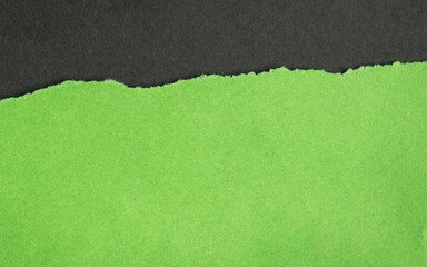 Torn green paper with rough edges on top of dark gray color paper.
