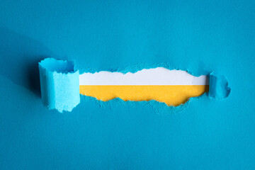 Torn blue paper with rough edges on top of white and yellow paper.