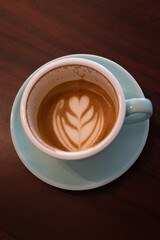 Cup of coffee with latte art on wooden table with soft sunlight. Perfect latte art on the bottom of cup.