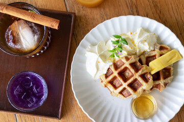 Delicious homemade waffles topped with cream and served with syrup and refreshing beverages on a...