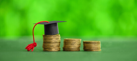 Stacks of coins with graduation hat on table outdoors. Student loan concept
