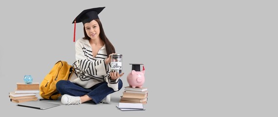 Female student in graduation hat and with savings for education on grey background with space for...