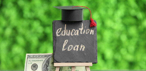 Chalkboard with text EDUCATION LOAN, graduation hat and dollar banknotes on table outdoors