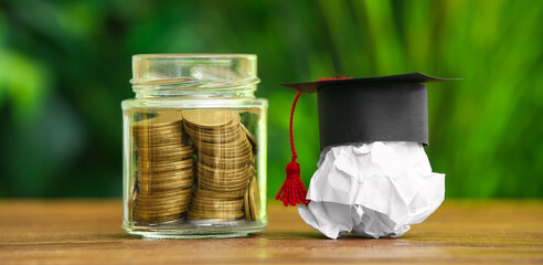 Crumpled paper with graduation hat and jar of coins on table outdoors. Student loan concept