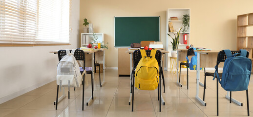 Interior of empty classroom with desks and backpacks on chairs