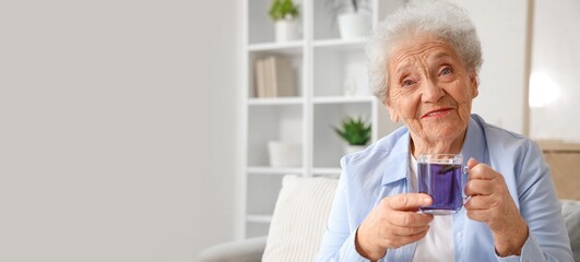 Fototapeta premium Senior woman with glass cup of butterfly pea flower tea in living room