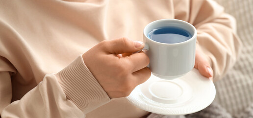 Woman holding cup of tasty blue tea at home. Closeup